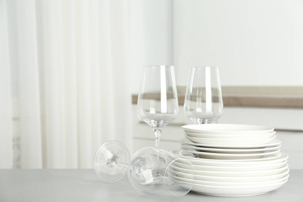 Stack of clean plates and glasses on grey table in kitchen. Space for text - Фото, изображение