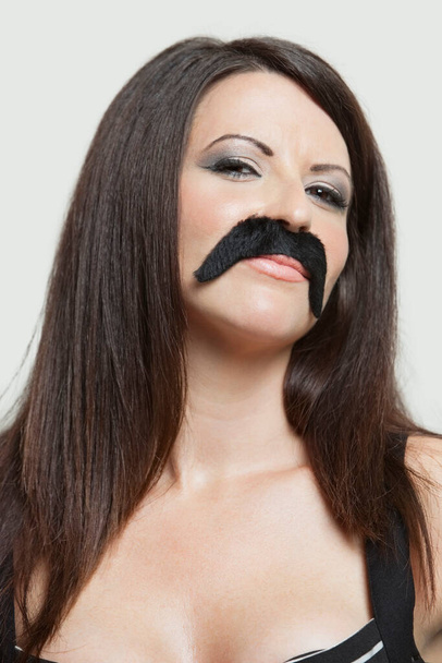 Портрет серйозної молодої жінки з підробленими вусами на сірому фоні
 - Фото, зображення