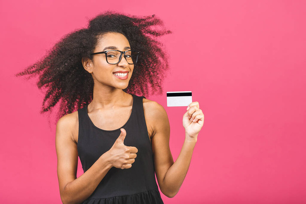 Imagem de uma bela jovem afro-americana animado emocional feliz mulher posando isolado sobre fundo de parede rosa segurando cartão de crédito. Polegares para cima
. - Foto, Imagem