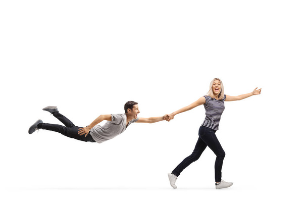 Full length profile shot of a happy young woman pulling a young man by the hand and running isolated on white background - Photo, Image