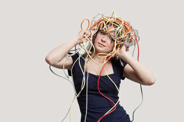 Young woman with head tangled in colorful cables over gray background - Fotoğraf, Görsel