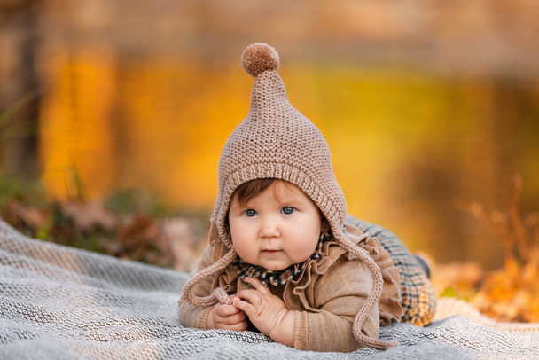 Beautiful baby girl sitting on the plaid near pond. Child outdoor. Baby at picnic in autumn park on sunny day. Pretty little girl - Фото, зображення
