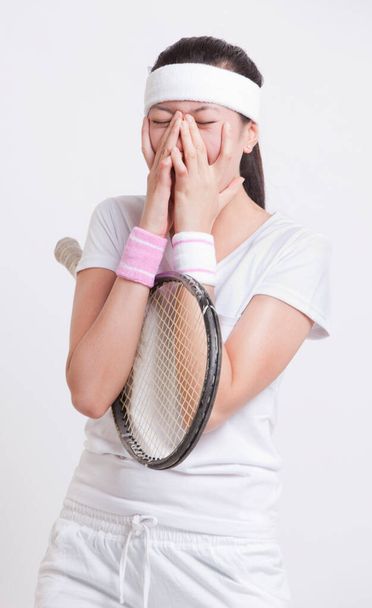 Young female tennis player with hands on face against white background - Фото, изображение