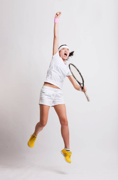 Young Asian female tennis player with racket jumping in excitement against white background - Zdjęcie, obraz