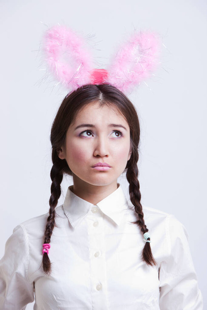 Contemplative Asian woman with bunny ears against white background - Фото, зображення