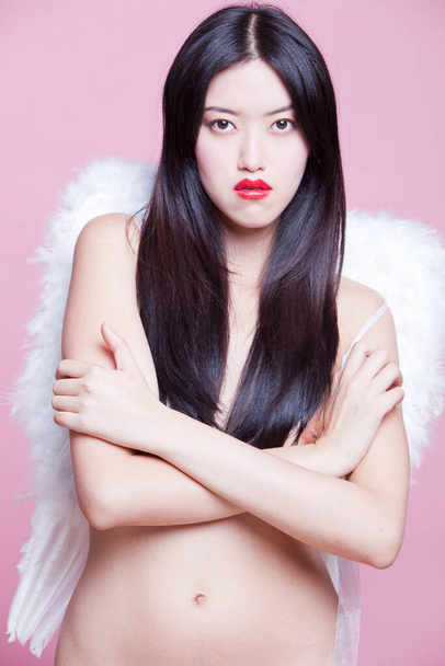 Portrait of young woman wearing angel wings against pink background - Foto, afbeelding