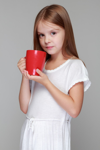 Little girl drinks tea from a red cup - 写真・画像