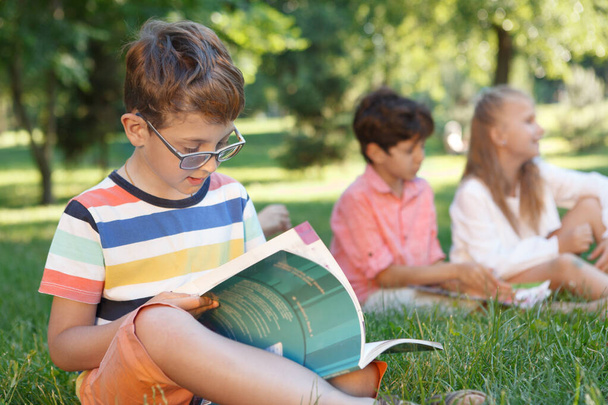 Aranyos kisfiú tanul a szabadban a barátaival a háttérben - Fotó, kép