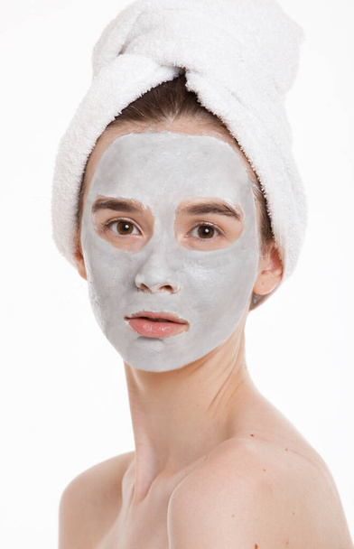 Portrait of young woman with face pack and towel wrapped around head against white background - Foto, Imagen