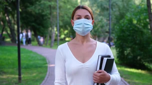 Portrait Student girl stands alone in a Park in a mask during the epidemic. Safety, distance, health, N1H1, virus protection, covid, virus and coronavirus concept. - Materiał filmowy, wideo