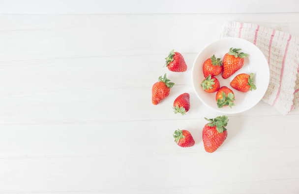Top view of fresh strawberries on a white rustic wooden table, inside a bowl ready to eat as organic and healthy food, next to a cloth with red stripes  - Photo, Image