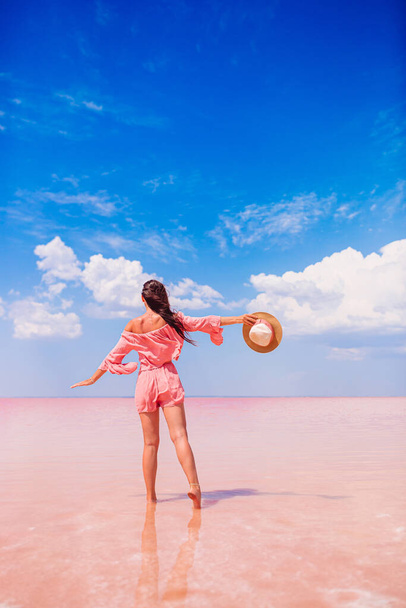 Mujer en sombrero caminar en un lago de sal rosa en un día soleado de verano. - Foto, imagen