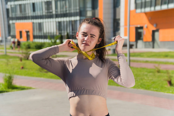 funny naughty girl holds a centimeter tape in her hands. The concept of improper weight loss woman fitness trainer in the park - Foto, immagini