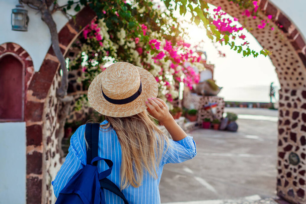 Woman traveler walks along traditional village architecture on Santorini island Greece. Tourist backpacker admires bougainvillea flowers - Zdjęcie, obraz