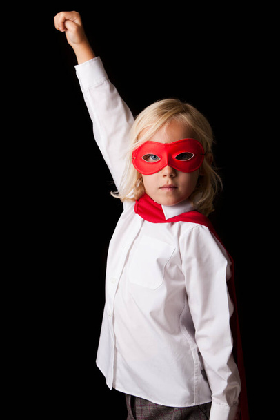 adorable blonde girl in red hero mask looking at camera on black background - 写真・画像