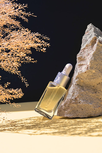 Bir şişe bitkisel masaj yağı. Siyah arka planda taş ve kurumuş çiçeklerden oluşan bir fotoğraf.. - Fotoğraf, Görsel