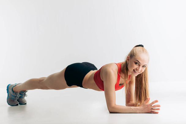 cheerful blonde athlete showing plank exercises for tight, flat abs - Fotó, kép
