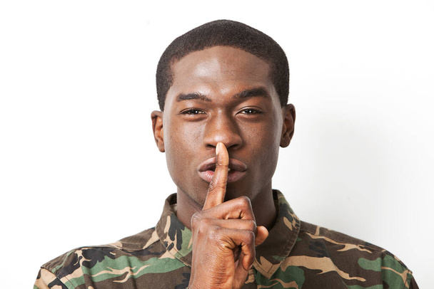 Portrait of young military soldier in camouflage clothing making silent gesture against white background - Foto, Imagem