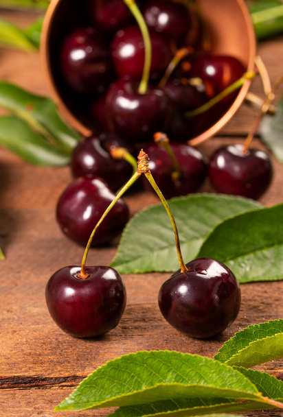Soczyste jagody słodkiej wiśni z liśćmi na drewnianym stole - Zdjęcie, obraz