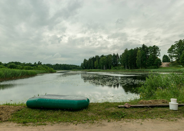 landschap met groene rubberboot aan de oever van het meer, visconcept, vrije tijd in de natuur, zomertijd - Foto, afbeelding