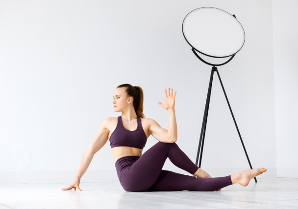 Atletische jonge vrouw doen twist stretching oefeningen op de vloer in een high-key fitnessruimte in een gezondheid en fitness concept om haar onderrug spieren te versterken en rek haar wervelkolom - Foto, afbeelding