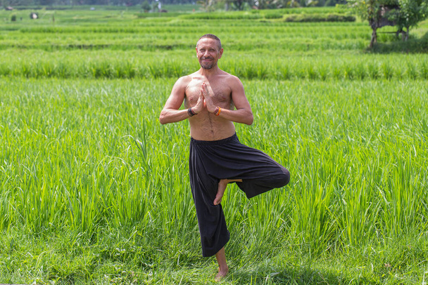 Man doing yoga and meditating in a position near a green rice field on the tropical island of Bali, Indonesia. Close up. The concept of a healthy lifestyle - Foto, Imagem