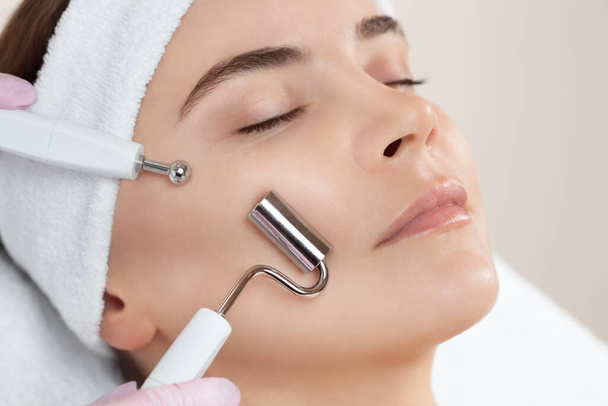 Kosmetolog sprawia, że aparatura jest zabiegiem terapii mikroprądowej pięknej, młodej kobiety w salonie piękności. Kosmetologia i profesjonalna pielęgnacja skóry. - Zdjęcie, obraz