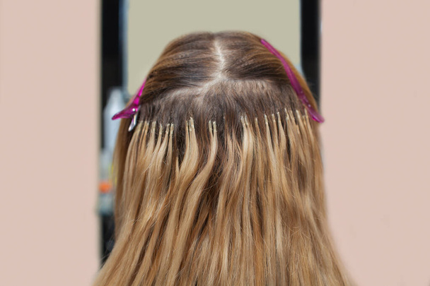 O cabeleireiro faz extensões de cabelo para uma jovem, uma loira em um salão de beleza. Cuidados com o cabelo profissional
. - Foto, Imagem