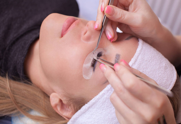 Makeup Master korrigiert und stärkt die Wimpernstrahlen, indem er in einem Schönheitssalon eine Pinzette hinhält. Professionelle Pflege für Haut und Augen. - Foto, Bild