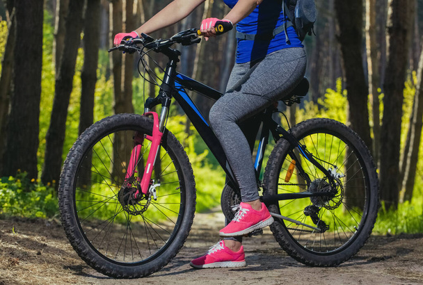 Eine junge Frau - eine Athletin in rosa Schuhen geht morgens mit dem Mountainbike durch einen Kiefernwald . - Foto, Bild