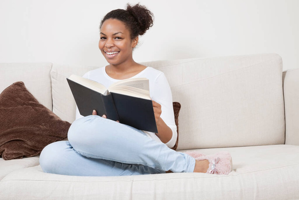 Happy young African American woman reading book on sofa - Фото, зображення