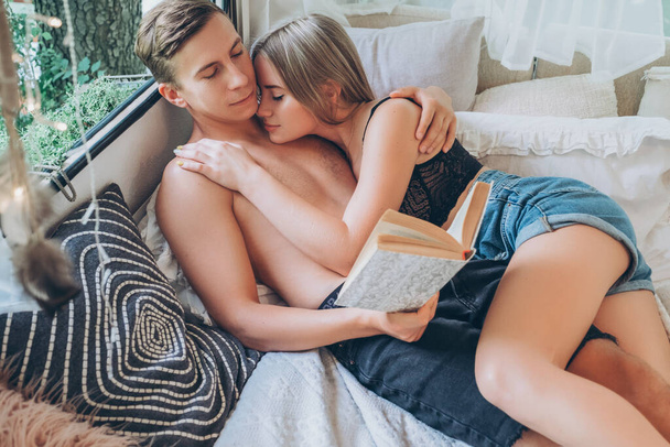 Junge verliebte Paare streicheln einander. Sie kümmern sich, küssen und umarmen sich liebevoll. Sommerporträt zu Hause auf dem Bett in lässigem Outfit. - Foto, Bild