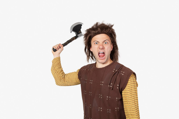 Portrait of angry young man in caveman costume holding axe against gray background - Φωτογραφία, εικόνα