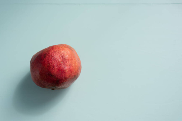 Nebroušené granátové jablko přes světle zelený stůl s kopírovacím prostorem - Fotografie, Obrázek