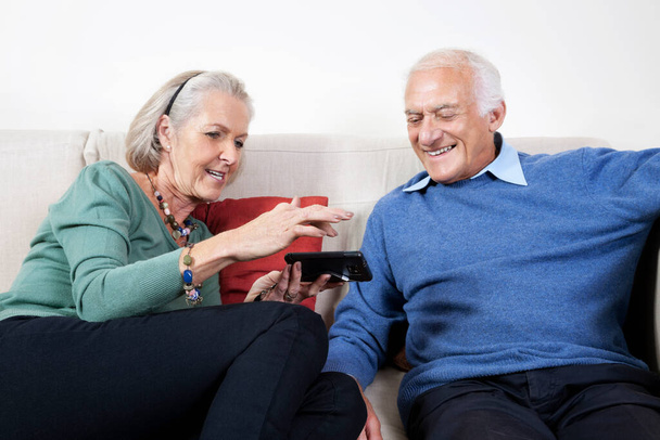 Happy senior couple using smart phone while sitting on sofa at home - Foto, immagini
