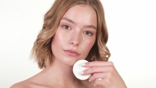 Beautiful tender young girl in a white home bathrobe with clean fresh skin posing in front of the camera with a sponge in her hands. Beauty face. Skin care. - Imágenes, Vídeo