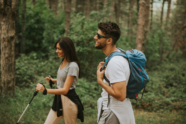 Улыбающаяся молодая пара, гуляющая с рюкзаками в лесу в летний день - Фото, изображение