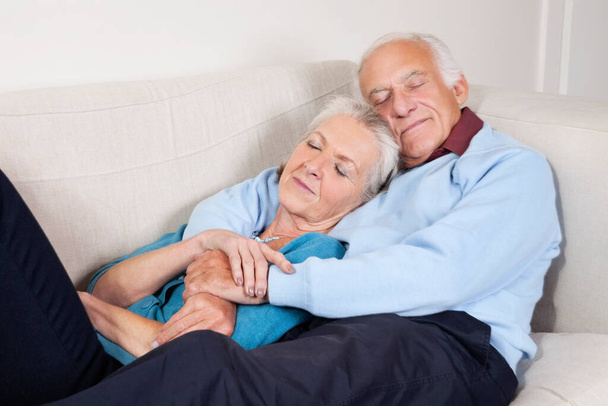 Romantic senior couple with arms around relaxing on sofa at home - Photo, image