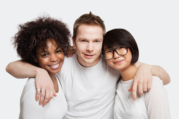 Portrait of young Caucasian man with his arms around two female friends over white background - Foto, imagen