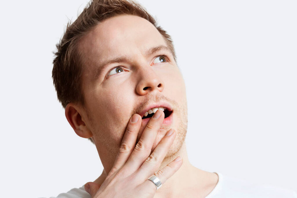 Contemplative young man with hand over mouth against white background - Foto, Imagen