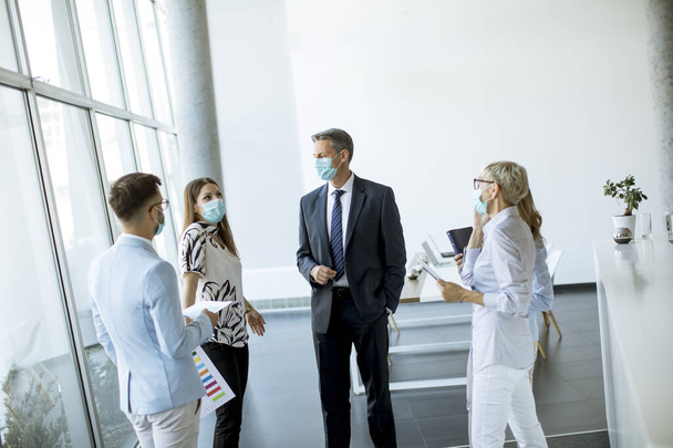 Бизнес-партнеры, стоящие и глядя на бизнес-результаты в офисе во время ношения маски SA защиты от вирусов - Фото, изображение