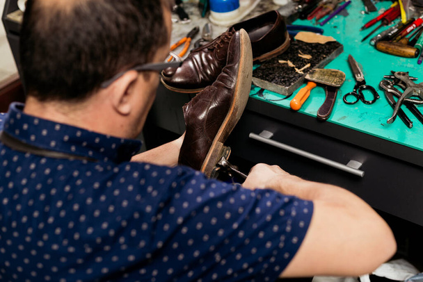 Male shoemaker using pliers to remove shoe sole. Cobbler at work.  - Photo, Image