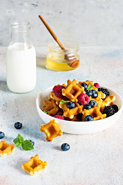 Apró (Mini) gofri gofri tejjel reggelire bogyókkal fehér tálban, könnyű háttérrel. - Fotó, kép