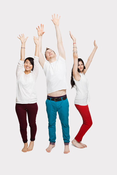 Multi-ethnic friends in casuals with arms raised standing together over white background - Foto, imagen
