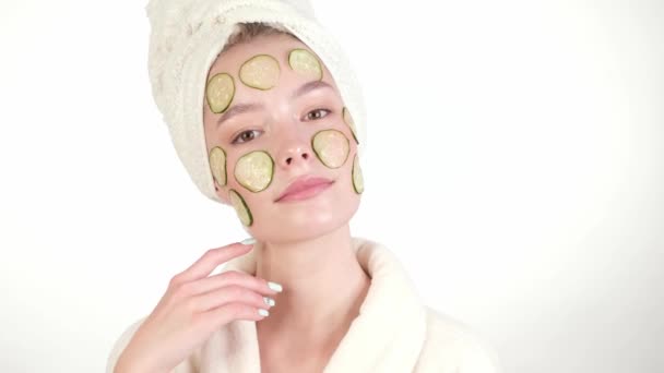 Beautiful tender young girl in a white towel with clean fresh skin posing in front of the camera with a mask of cucumbers on the face. Beauty face. Skin care. - Záběry, video