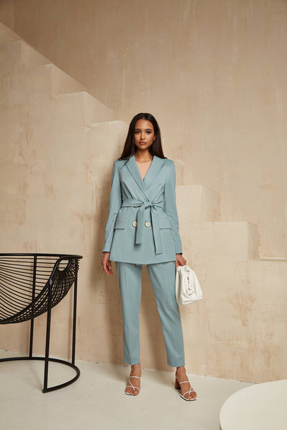 Beautiful brunette woman natural make up wear fashion clothes casual dress code office style blue jacket and pants suit for romantic date business meeting accessory bag interior boho stairs flowerpot. - 写真・画像