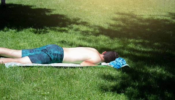 jovem dormindo na grama e tomando banho de sol com o perigo de não ter qualquer proteção solar no verão
 - Foto, Imagem