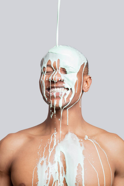 Paint falling on happy shirtless young man's head against gray background - Фото, зображення