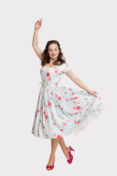 Porträt einer schönen jungen Frau in einem Kleid, das in Tanzpose vor weißem Hintergrund steht - Foto, Bild