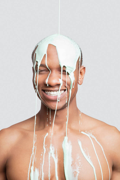 Молодой человек без рубашки с краской падает на голову на сером фоне - Фото, изображение